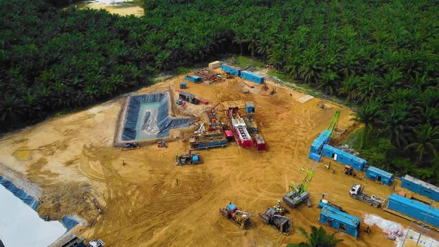 Cinematic Drone Footage of Onshore Drilling Rig equipment structure for oil exploration and exploitation in the middle of jungle surrounded by palm oil trees during sunset and high oil price.