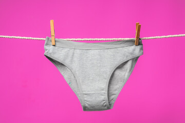 Female panties hanging on rope against pink studio background