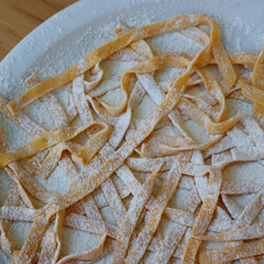 Homemade italian traditional pumpkin Tagliatelle pasta on a plate with flour on wooden table. Raw itialian pasta also called fettuccine, tagliatelle or pappardelle