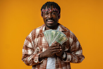 Obraz premium Young happy rich african man in casual shirt holding dollar bills against yellow background