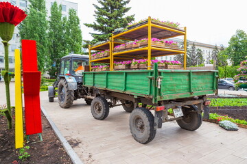 Obraz premium tractor with a trailer stands on the sidewalk with boxes of flowers for planting in the city lawn