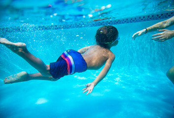 Young diverse boy swimming underwater in a swimming pool. Learning to swim with the help of his...