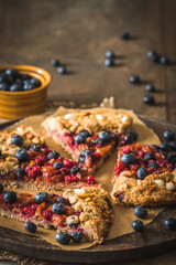 Pieces of a berry galette with fresh blueberries on a rustic wooden table, vertical