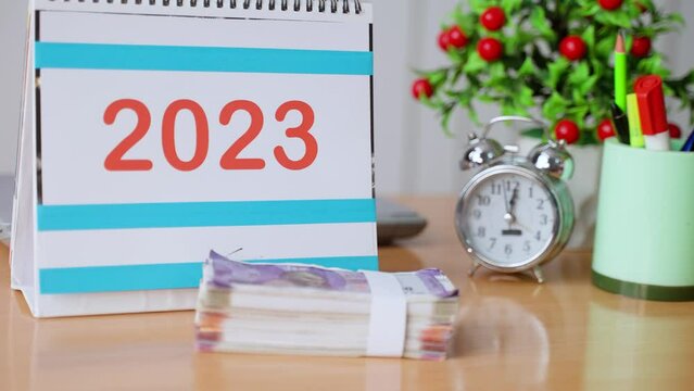 handheld close up shot of hands placing Money bundle in front of 2023 calendar - concept of new year budget, investment planning and taxation
