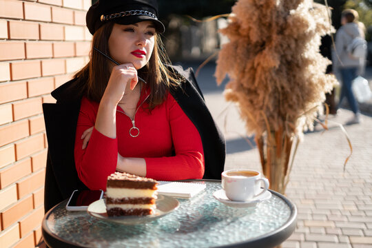 beautiful stylish young woman sit in cafe and drink coffee or tea with cake, street front view.