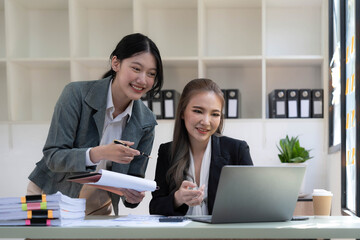 Two young Asian business woman talk, consult, discuss working with new startup project idea presentation analyze plan marketing and investment in the office.