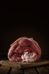 one raw meaty pork knuckle on cutting board and old boards on a soft brown wooden backdrop. artistic moody photo in simple rustic style with copy space