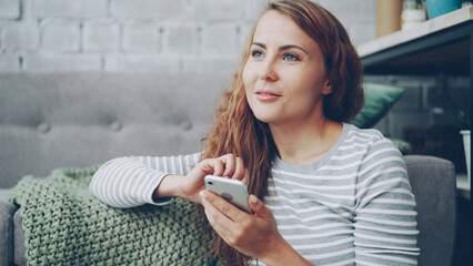 Happy young woman is holding smartphone touching screen and smiling checking social media account or reading text messages. Modern technology and millennials concept.