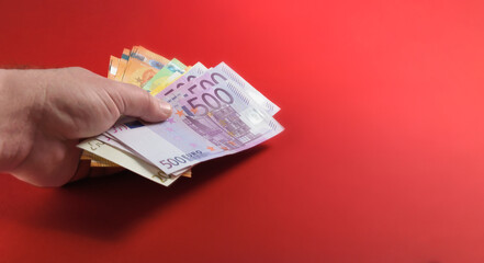 Cash money in a man's hand on a red table background. Hand holding euro banknotes banner