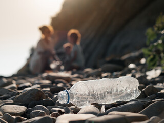 Little siblings helping mother to collect garbage on sea beach blurred on the background of plastic...