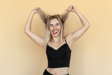 Cheerful caucasian young woman grimacing, fooling and making funny faces during photoshoot. Studio shot of pretty girl fooling around on beige background. Humor concept