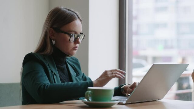attractive businesswoman is typing message on laptop keyboard in cafe, sending emails to partners