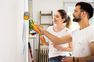 Smiling young couple painting wall in their home together.