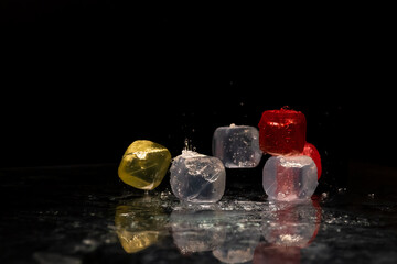 Falling colored cubes splashed with water on a black background. Red, yellow, blue and transparent. Conceptual, celebrated, commercial design