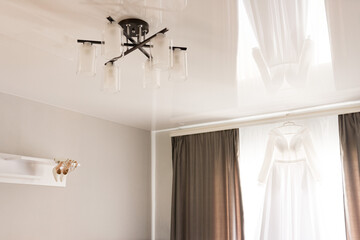 the wedding dress is hanging on the background of the window and the bride's shoes are on the shelf.