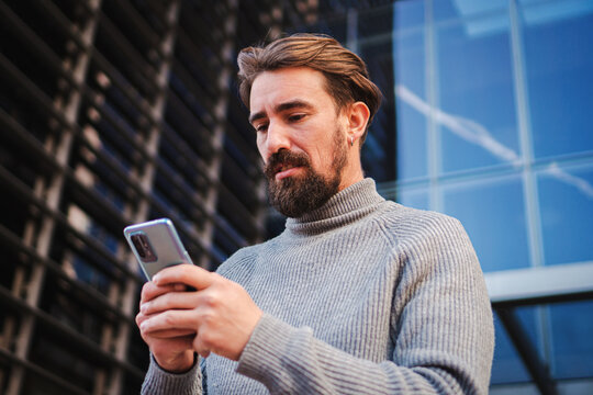 Serious young man concentrated and concerned using a mobile phone app texting and sharing media on a workspace. High quality photo