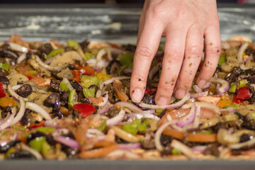 Preparing home made vegeterian pizza with onions, black olives, green and red peppers and mushrooms in a pan