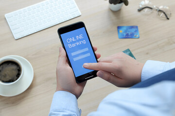 Man using online banking app on smartphone at wooden office table, closeup