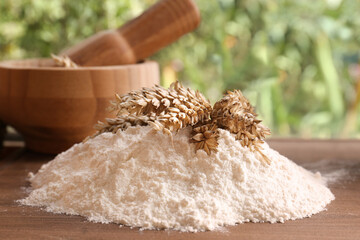 Pile of wheat flour and spikes on wooden board indoors, closeup
