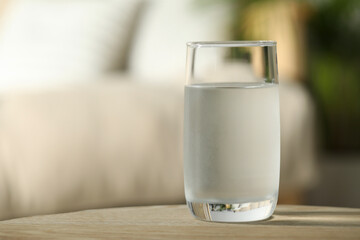 Glass of pure water on wooden table against blurred background, space for text
