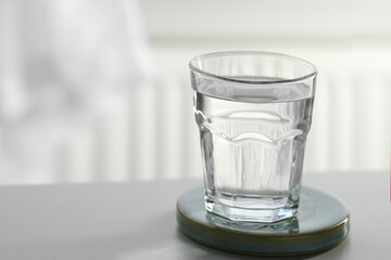 Glass of pure water on light table against blurred background, space for text