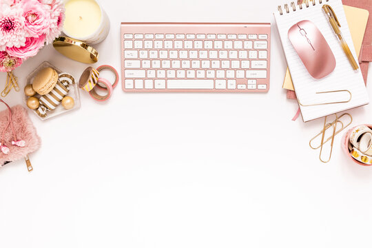 A femininely styled desktop in shades in gold and dusty pink with modem stationery. Lifestyle theme inspired by the office workspace of a stylish woman. Flat lay with fresh flowers pink keyboard and