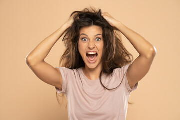 Angry nervous woman pulling her messy long hair on a beige background