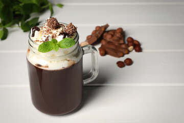 Mason jar of delicious hot chocolate with whipped cream and mint on white wooden table. Space for...