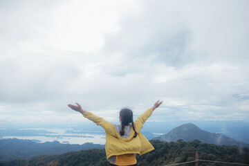 Woman standing on cliff and see over view in nature. Tourist show  hands up and enjoying fresh air. Woman enjoying free happiness in beautiful Thailand landscape.