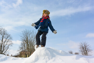 Fototapeta na wymiar Boy, jumping, having fun on a snowy winter park. Happy boy outdoors. A boy plays outside in winter. Winter fun activity outdoor, winter vacation. Family time
