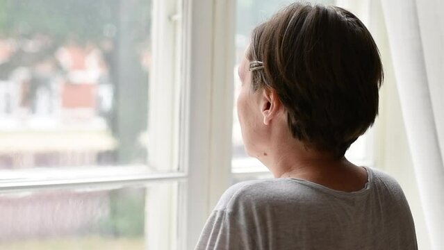 Introspective mid-adult female person looking out the window and contemplating