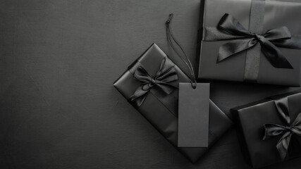 Gift box wrapped in black paper with a black bow on a dark background. Holiday concept. Black...