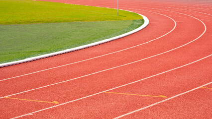 Curve lines pattern background of red synthetic running tracks and green field in athletic outdoors stadium