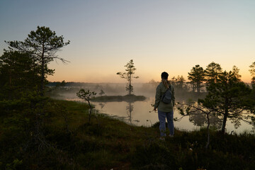woman tourist meets dawn in nature. Sunset,  light and fog, Reflections of trees in lakes . Travel romance. Viru swamps Estonia.