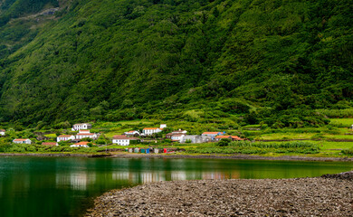 Small village by the lake under the steep volcanic hill. Sao Jorge island, Azores, Portugal. 