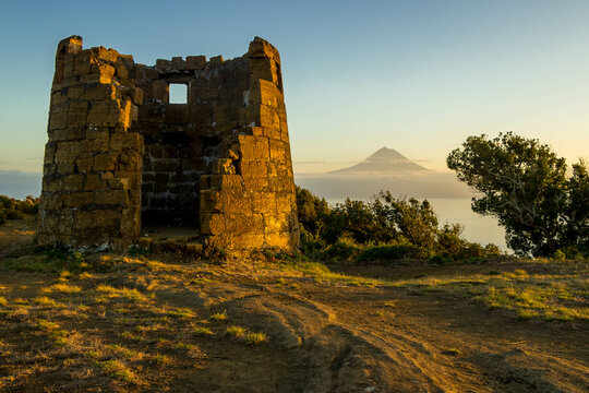 Ruins of an old watch tower at sunset. Pico volcanic mountain, highest mountain of Portugal, in the background. 