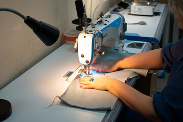 There is a professional sewing machine on the table, female hands hold the fabric and sew the product on the sewing machine.