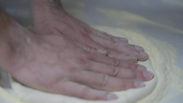 Slow motion close-up of laying out pizza dough by hand.