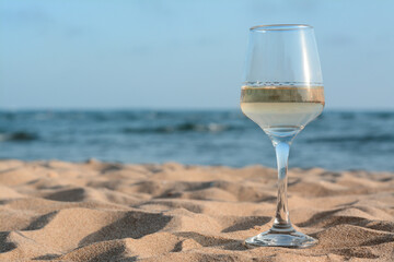Glass of tasty wine on sand near sea, space for text