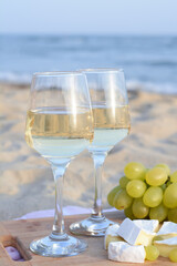 Glasses with white wine and snacks for beach picnic on sandy seashore