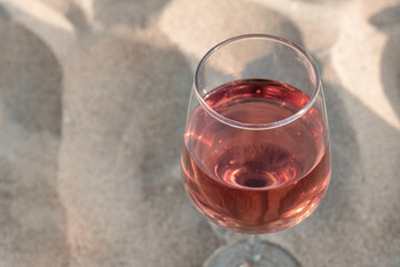 Glass of tasty rose wine on sand, closeup. Space for text