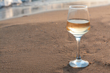Glass of tasty wine on sand near sea, space for text