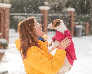 Caucasian woman hugging with dog while walking in winter. Jack Russell Terrier in a warm pink...
