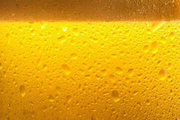 Glass of tasty cold beer with foam and condensation drops as background, closeup