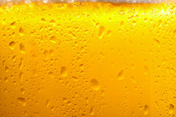 Glass of tasty cold beer with foam and condensation drops as background, closeup