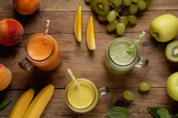 Mason jars of different tasty smoothies and fresh ingredients on wooden table, flat lay