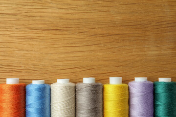 Many colorful sewing threads on wooden table, flat lay. Space for text