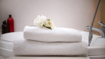 Fototapeta na wymiar Stacked bath towels and beautiful flowers on table in bathroom