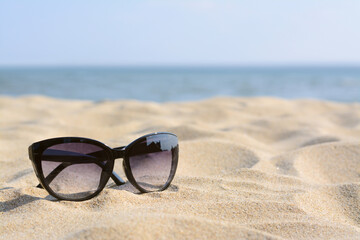 Fototapeta na wymiar Stylish sunglasses on sandy beach near sea, space for text