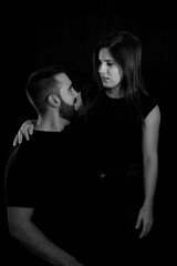 Portrait of a young couple in black and white with black background looking into each other's eyes.
